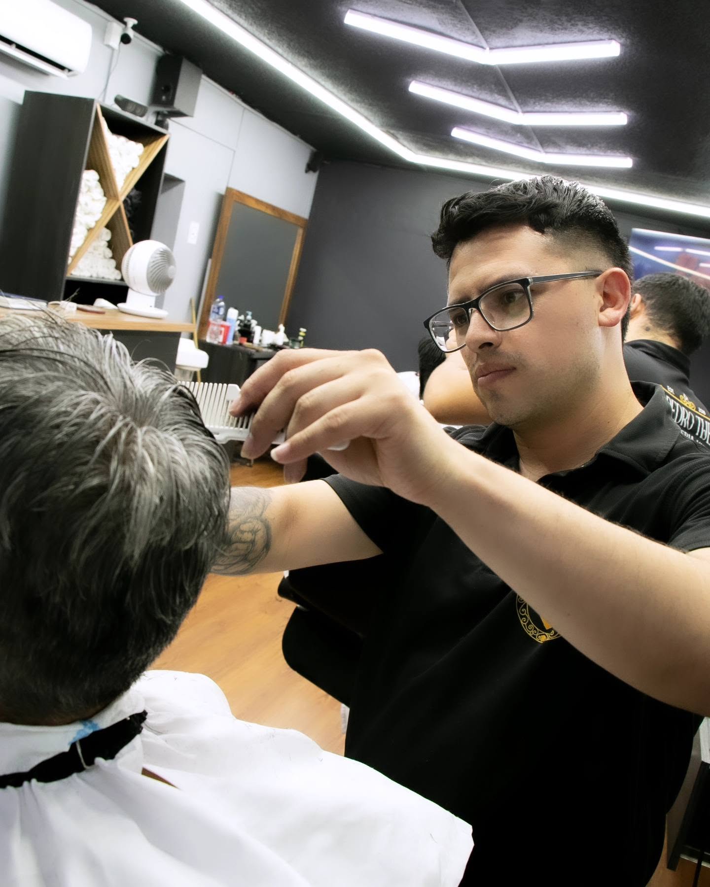 Barbero con lentes peinando y midiendo con los dedos el cabello cano de un cliente en la sala principal
