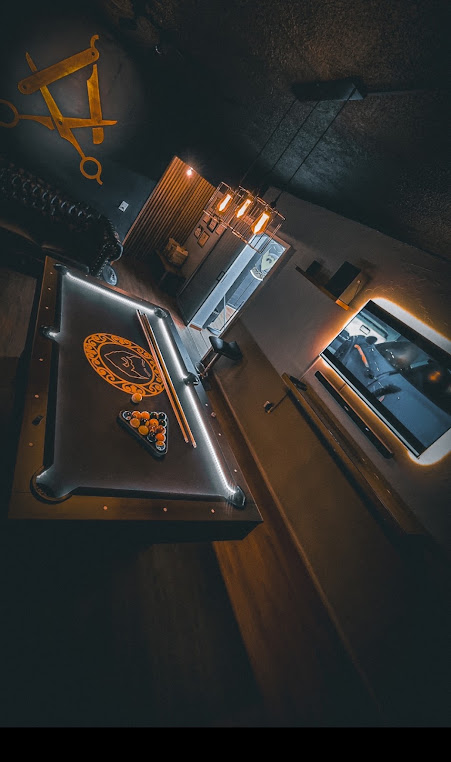 Mesa de billar con el emblema dorado de Mr. Pedro sobre el paño, bolas acomodadas y lámparas cálidas colgantes en la sala de espera